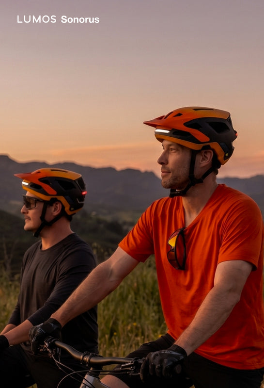 Two riders wearing orange Lumos Sonorus mesh intercom helmets in the hills at sunset